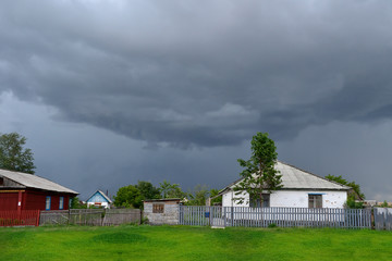 Two village houses, white and red, against the background of huge clouds on a cloudy day in summer