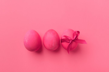 Bright pink eggs with satin bow on a pink background. Festive spring concept. Color trend.