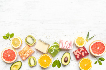 Top view of various colorful handmade organic soaps arranged with citrus fruits, herbs, chia seeds and aloe. White rusric background, copy space.