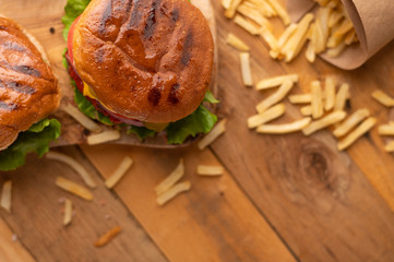 Fresh hot juicy burger with salty french fries. Meal on a cutting kitchen board on a wooden table. Tasty cheeseburger with beef, cheese and vegetables. American cuisine. Top view. Cooking food concept