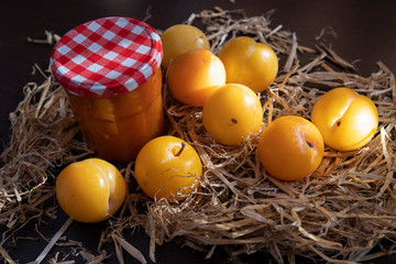 Close-up of yellow plums and a jar of jam in straw
