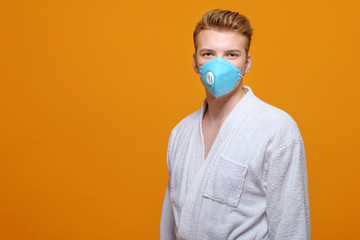 young man in medical mask and housecoat in quarantine on yellow orange background