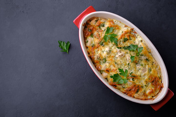 Baked chicken and vegetables in red casserole on black stone background with copy space. Flat lay composition