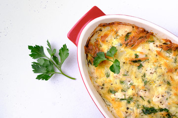 Baked chicken and vegetables in red casserole on white concrete background. Flat lay composition