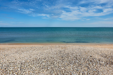 Fototapeta na wymiar Seascape - sea, blue sky and white clouds, beach with sea shells. Space for text.