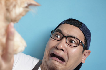 Fototapeta premium Man afraid of cat, funny face of a young Asian male scared or intimidated by kitten