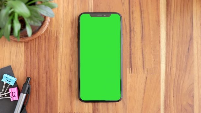 Smart Phone Place On Table Wood With Green Screen, Close-up The Cell Phone Is On The Brown Desktop, Man's Finger Slide Up Or Down Display Mobile Phone With Chroma Key.