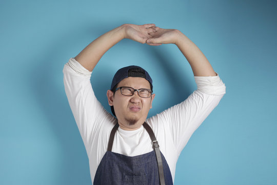 Portrait of male Asian chef or waiter stretching his arms, tired expression