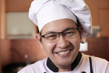 Portrait of happy proud Asian chef smiling at camera, chef in the kitchen