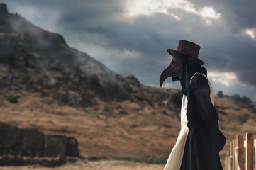 A man in historical masquerade costume of plague doctor in old gothic grange building of church....