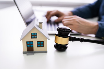 House Model With Gavel In Front Of Businessperson Using Laptop