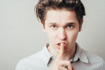  young man showing silence gesture, hand over mouth