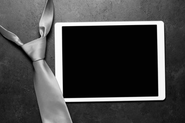 Men's tie and tablet. Black concrete background. Copy space