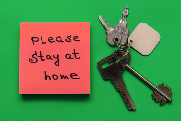 Bunch of keys and pink sticker with the inscription PLEASE STAY AT HOME on a green background.Concept of self isolation and home quarantine from coronavirus.