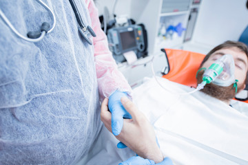 Ambulance interior, doctor with blue gloves takes hand to patient, while breathing oxygen. Emergency concept.