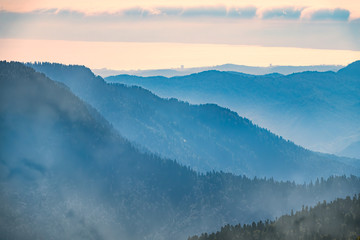 Naklejka premium Green mountain slope. Layers of mountains in the haze during sunset. Krasnaya Polyana, Sochi, Caucasus, Russia.