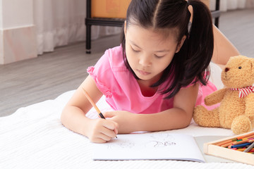Asian home school elementary adorable kids lie down on floor, drawing homework with color pencils, happy cheerful girl spent time concentrate  drawing quarantine period before back to school
