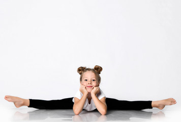 Smiling kid girl does gymnastic exercises at home splits bend forward with her head leaning her...
