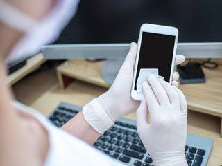 Asian women work at home using notebook, use alcohol pad to clean smartphone and prevent spreading of coronavirus during crisis of covid-19. Work from home and social distancing concept © peenat