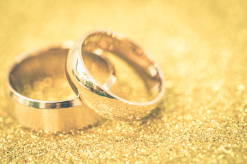 Gold wedding rings of bride and groom on gold gliter