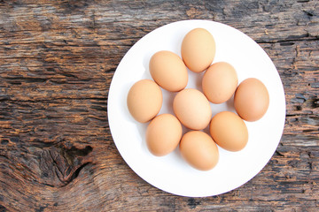 Fresh brown eggs in white plate on wooden background. Top view. Rural still life, natural organic healthy food concept. Copy space.