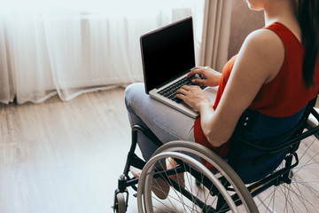 Woman in a wheelchair at home with a laptop on her lap, hand close up, unrecognizable man.