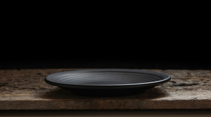 Black plate on wooden black background.