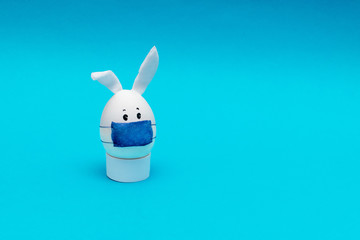 Easter egg with eyes,rabbit ears and a protective mask on a blue background. Coronavirus epidemic...