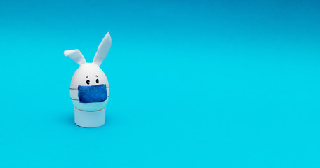 Easter egg with eyes,rabbit ears and a protective mask on a blue background. Coronavirus epidemic concept. Concept celebrating Easter in self-isolation and quarantine