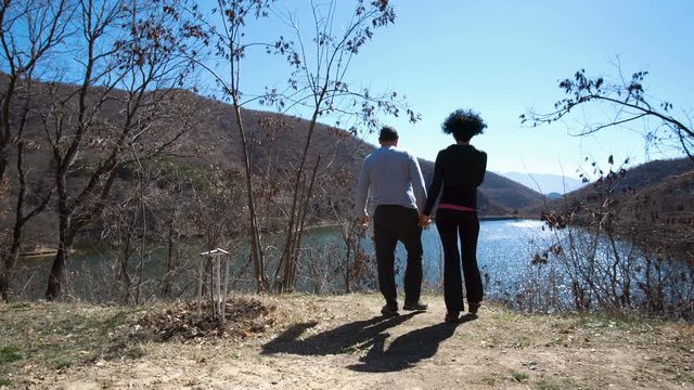 Rear view of a happy couple standing together outdoors near the lake and enjoying the view
