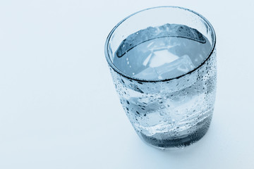 glass of water with ice cubes on a light background.