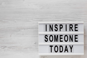 'Inspire someone today' words on a lightbox on a white wooden surface, top view. Overhead, from above, flat lay. Space for text.