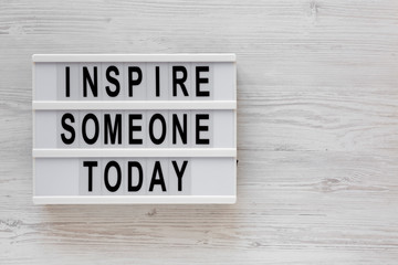'Inspire someone today' words on a lightbox on a white wooden surface, top view. Overhead, from above, flat lay. Copy space.