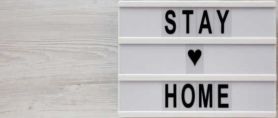 'Stay home' words on a lightbox on a white wooden background, top view. Overhead, from above, flat lay. Copy space.