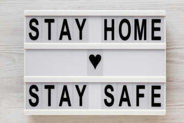 'Stay home stay safe' words on a lightbox on a white wooden background, top view. Overhead, from...