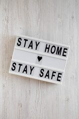 'Stay home stay safe' words on a lightbox on a white wooden surface, top view. Overhead, from above, flat lay.