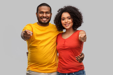 relationships and people concept - happy african american couple pointing to camera over grey background