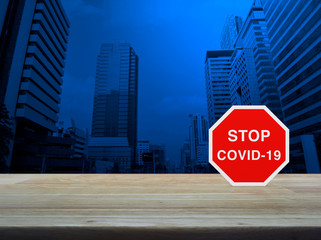 Stop COVID-19 outbreak icon plate on wooden table over modern office city tower and skyscraper,...