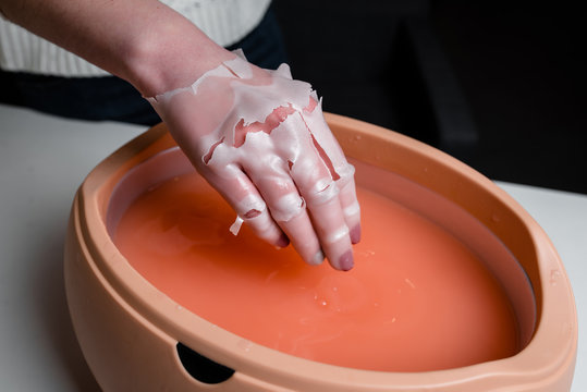 Female hand and orange paraffin wax in bowl. Manicure and skincare. Woman girl in beauty spa salon.