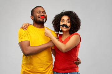 fun, photo booth and people concept - happy african american couple with party props hugging over...