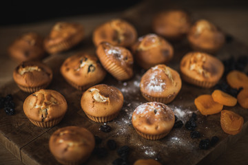 Obraz premium Freshly baked muffins with raisins and dried apricots, shot on a dark background. Background for baking and cooking.