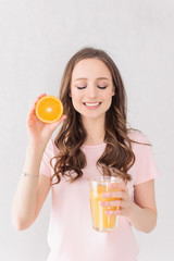 Attractive female in rose t-shirt holding orange and orange juice over white background
