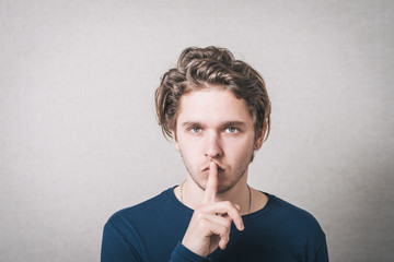 Man shows his finger to his mouth quiet. Gray background.