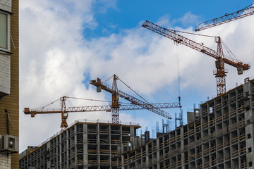 Construction site with cranes. High-rise construction cranes and a lot of unfinished buildings. Construction of multi-apartment modern houses and a new residential complex. Blue sky.