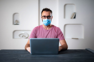 Freelancer with medical protective mask working from home in the days of pandemic and social distancing.