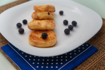 Traditional syrniki or cottage cheese pancakes with blueberries on white plate with blue napkin on kitchen table, close up.