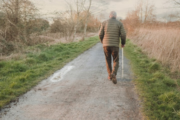 Old seniour man with grey hair walking on a foot path with metal cane. Concept outdroor activity,...