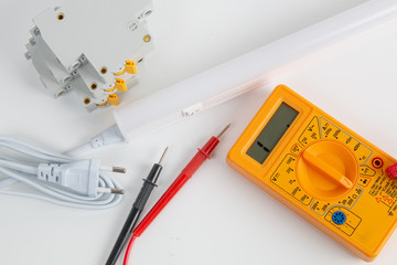 Digital multimeter, LED lamp and circuit breaker on white table. Top view