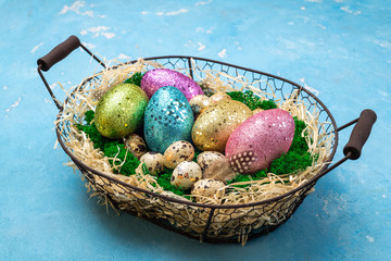 Spring Easter background for spring holidays. Easter composition with colorful Easter eggs on moss in basket on blue table. Top view