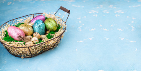 Spring Easter background for spring holidays. Easter composition with colorful Easter eggs on moss in basketon blue table. Top view, copy space
